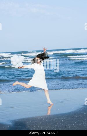 Springende Frau mit weißen Balonballen am Strand am Meer Stockfoto