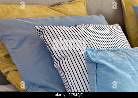 Nahaufnahme von gelben und hellblauen Kissen in einer Reihe auf dem Bett, moderne Retro-Dekoration für zu Hause, Pastell hellen Farben bunt hell Stockfoto