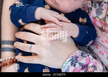 Selektive Fokusaufnahme der kleinen Hände eines Säuglings, die auf seiner Mutter ruhen, die schützenden Finger breiteten sich in einer schützenden Pose über seinen Magen aus Stockfoto