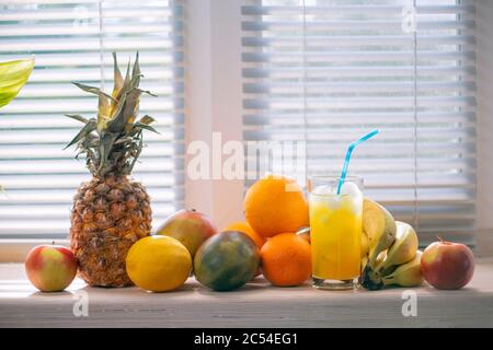 Die Früchte liegen auf einer von der Sonne beleuchteten Fensterbank: Ananas, Bananen, Zitrone, Mango und Juce mit Eis Stockfoto