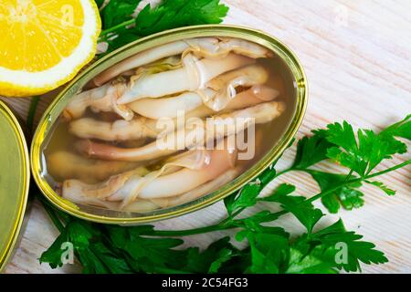 Meeresfrüchte. Salzwasserkonserven ensis in offener Blechdose auf Holztisch mit Zitrone und Grünpflanzen Stockfoto