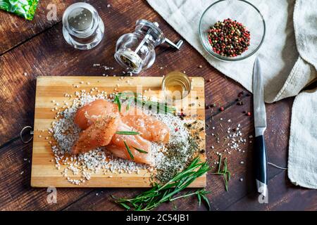 Hühnerrucky liegt auf einem Brett mit Gewürzen und Meersalz. Rosmarin, Kardamom, Pfeffer. Stockfoto