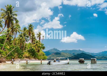 Schöner tropischer Strand mit Palmen, Steg, Touristenboot und weißen Wolken darüber. Urlaub und Paradies Insel Urlaub Konzept. Stockfoto