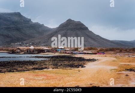 Geheimnisvolle Landschaft mit sandiger Küste mit Fischerdorf und schwarzen vulkanischen Bergen im Hintergrund. Baia Das Gatas. Nördlich von Calhau, Sao Vicente I. Stockfoto