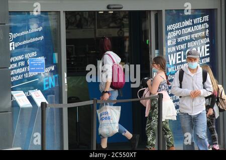 Eine Familie, die in einen Laden geht, und ein Mann, der Gesichtsmasken trägt Stockfoto