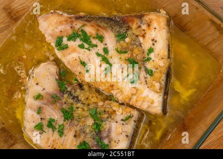 Schwertfisch-Spieße mit Zitronenbutter-Sauce und Petersilie. Zwei Fischpfähle schließen in einer Glasschale direkt von oben Stockfoto