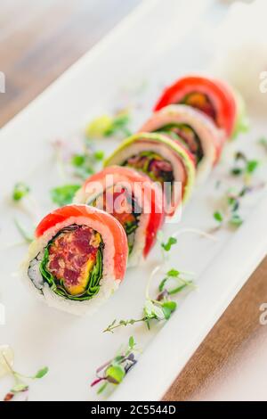 Japanische Uramaki Sushi-Rolle. Eine Uramaki-Sushi-Rolle auf einem weißen Teller. Der rohe Sashimi Thunfisch und Reis sind draußen, während Nori drinnen ist. Diese de Stockfoto