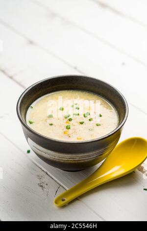 Maissuppe und gelber Löffel. Ein kantonesisches Gericht, das in chinesischen Restaurants oft als Vorspeise serviert wird. Die Schüssel mit Suppe ist auf weißem Hintergrund. Ei Stockfoto