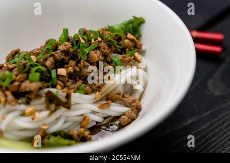 Dan Dan Noodles Nahaufnahme. Dan Dan Noodles ist ein würziges Szechuan-Gericht, das häufig in chinesischen Straßenessen zu finden ist. Zutaten sind dicke Reisnudeln Stockfoto