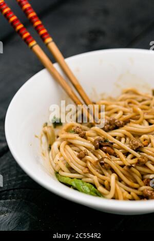 Dan Dan Noodle Vertikale Ansicht. Dan Dan Noodles ist ein würziges Szechuan-Gericht, das häufig in chinesischen Straßenessen zu finden ist. Zutaten sind dick Reis n Stockfoto