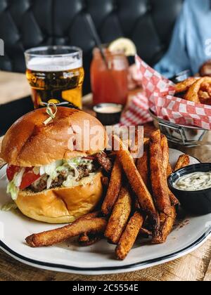 Hamburger mit pommes frites. Ein klassisches amerikanisches Gericht, das in Fast Food, Gourmet-Restaurants und zu Hause serviert wird. Frisch geschnittene pommes Frites als Beilage und ein Stockfoto