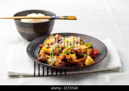 Süßes und saures Schweinefleisch mit Reisschüssel. Frittiertes Fleisch wird hinzugefügt, um gebratene Ananas, Zwiebeln, Paprika und Sauce zu rühren. Süsse und saure Gerichte sind in einem häufig Stockfoto