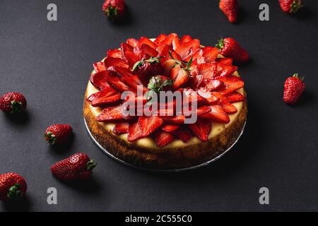 Erdbeer Käsekuchen auf dunklem Hintergrund. Dieser süße und köstliche hausgemachte Käsekuchen ist ein klassisches dekadentes Dessert und wird mit frischem Strohgebäck gekrönt Stockfoto