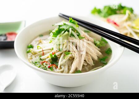 Vietnamesische Pho Nudelsuppe Schüssel Nahaufnahme. Diese Pho-Suppe ist ein klassisches, authentisches vietnamesisches Essen und wird in einer weißen Schüssel mit Hühnerbrühe und viel f serviert Stockfoto
