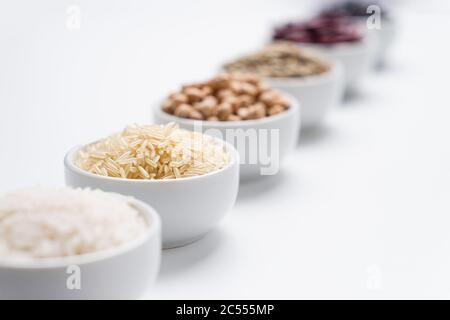 Getreide von Reis und Bohnen Hintergrund. Geringe Schärfentiefe auf Basmati-Reiskörnern in einer weißen Schüssel mit anderen Arten von Reisgetreide und Bohnenleguminosen b Stockfoto