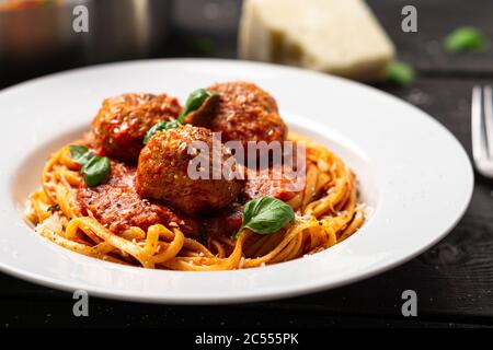 Spaghetti und Fleischbällchen Teller Nahaufnahme. Italienische Pasta-Gericht in weißen Teller auf schwarzem Holzhintergrund serviert. Spaghetti und Fleischbällchen sind wie Bolognese Stockfoto