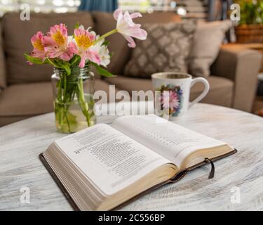 Horizontale Aufnahme eines Buches auf einem Couchtisch Mit einem Becher und Blumen auf einem braunen Couchhintergrund Stockfoto