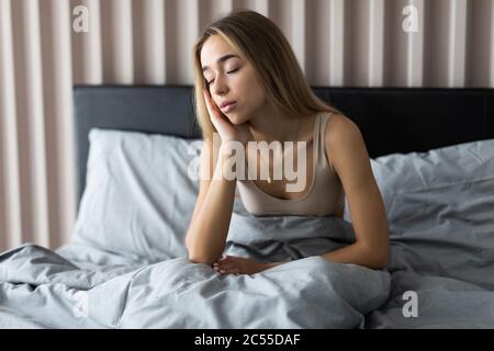 Schläfrige junge Frau, die sich nach dem Aufwachen im Bett schläfrig oder schwindelig fühlt, an Schlaflosigkeit, Schlaflosigkeit, Morgenkopfschmerz oder Migräne leidet Stockfoto