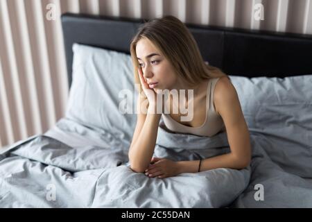 Schläfrige junge Frau, die sich nach dem Aufwachen im Bett schläfrig oder schwindelig fühlt, an Schlaflosigkeit, Schlaflosigkeit, Morgenkopfschmerz oder Migräne leidet Stockfoto