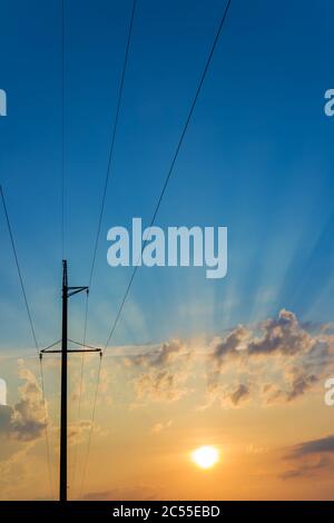 Hochspannungsmasten gegen schönen Himmel mit Sonnenstrahlen. Elektrische Pole Power Lines und Wolken. Stockfoto