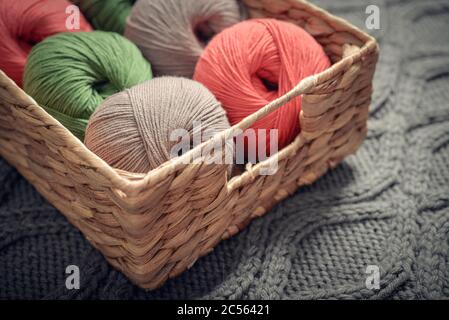 Farbige Garnkugeln in rustikalem Weidenkorb auf blauer Couch in Nahaufnahme Stockfoto