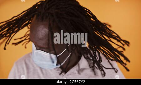 Afrikanischer Mann mit Gesichtsmaske schüttelt seine geflochtenen Haare. Stockfoto