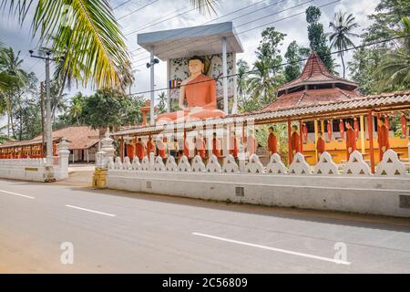 Viele Statuen buddhistischer Mönche stehen in einer langen Reihe vor einer großen Buddha-Statue an einer Wand, Sri Lanka Stockfoto