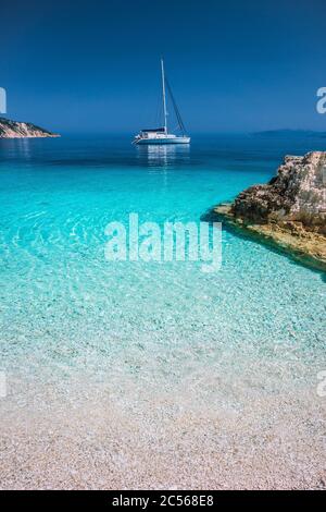 Urlaubsurlaub. Azure blaue Lagune mit ruhigen Wellen und treibenden Segelkatamaran-Yacht-Boot mit Küstenlinie im Hintergrund. Stockfoto