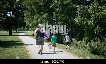 Vater mit Zopf geht mit seinen beiden Jungen, wie sie zu ihrem Lieblings-Angelplatz fahren, mit Stöcken und einem großen Fischnetz an einem sonnigen Tag in Ontario. Stockfoto