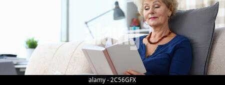 Ältere Frau sitzt zu Hause auf dem Sofa und liest Buch Stockfoto