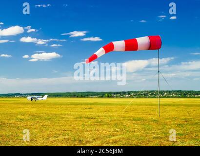 Rot-weiße Windsack Wind Socke auf blauen Himmel auf dem Flugplatz, gelbe Feld und Wolken Hintergrund Stockfoto