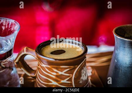 Keramik-Tasse mit starkem schwarzen türkischen Kaffee, alten Cezve Kaffee türkischen Topf und ein Glas kaltes Wasser. Selektiver Fokus. Stockfoto