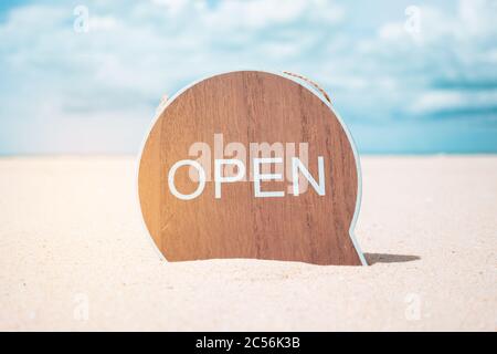 Jetzt offene Schild stehen auf Sand Sommer Strand Hintergrund Metapher zu Zeit zu reisen entspannen Tourismus Saison mit Copyspace Hintergrund. Stockfoto