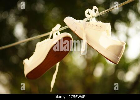 Weiße Turnschuhe werden nach dem Waschen an einem Seil in einem Sommergarten getrocknet. Stockfoto
