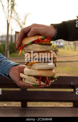 Selektive Fokusaufnahme von zwei männlichen Händen, die die Reihe drücken Von drei Burgern Stockfoto