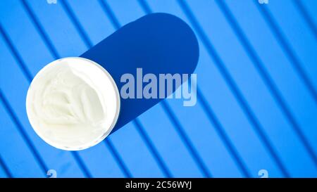 Weiße Creme in einer Schüssel auf blauem Hintergrund mit tiefem Schatten, Glas Creme auf blauem Hintergrund mit einem Schatten Stockfoto