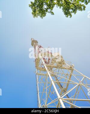 Rot-weißer Turm der Kommunikation mit mit vielen verschiedenen Antennen unter klarem Himmel. Stockfoto
