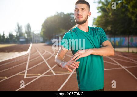 Junger Mann in kabellosen Ohrhörern überlegt beiseite, Zeit auf dem Laufband des Stadions isoliert zu verbringen Stockfoto