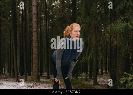 Läuferin, die sich mit Händen auf Knien in verschneiten Wäldern ausruhte Stockfoto