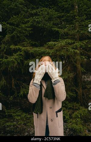 Portrait verspielte Frau mit Fäustlingen über Gesicht in Holz Stockfoto