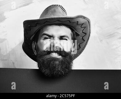 Bärtiger Mann, langer Bart. Brutal kaukasisch lustig unrasiert Hipster in vintage Cowboy Hut mit blauem Papier Blatt im Studio auf bunten Hintergrund Stockfoto