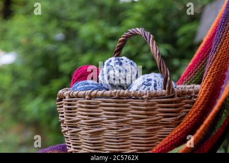 Bunte Kugeln aus Strickgarn in einem Korb auf einem Hintergrund von grünen Zweigen der Fichte. Horizontales Poster mit Platz für Kopien. Garn zum Stricken. Stockfoto