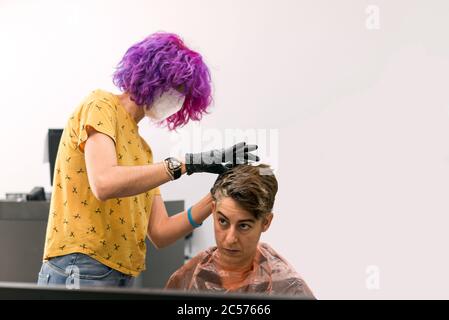 Konzept: Entbindung nach Coronavirus, covid-19. Professioneller Friseur mit Gesichtsmaske und Handschuhen. Färben der Haare und setzen blonde Highlights Stockfoto