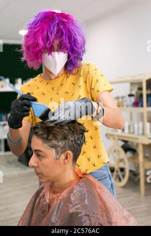 Konzept: Entbindung nach Coronavirus, covid-19. Professioneller Friseur mit Gesichtsmaske und Handschuhen. Färben der Haare und setzen blonde Highlights Stockfoto