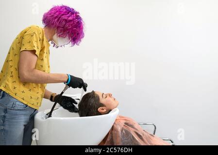 Konzept: Entbindung nach Coronavirus, covid-19. Professioneller Friseur mit lila Haaren. Waschen Sie den Kopf einer Frau nach dem Schneiden ihrer Haare, färben Stockfoto