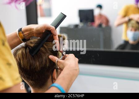 Konzept: Entbindung nach Coronavirus, covid-19. Detail der professionellen Friseur Hände. Schneiden Haare braun kurze Haare Frau beim Friseur. Stockfoto