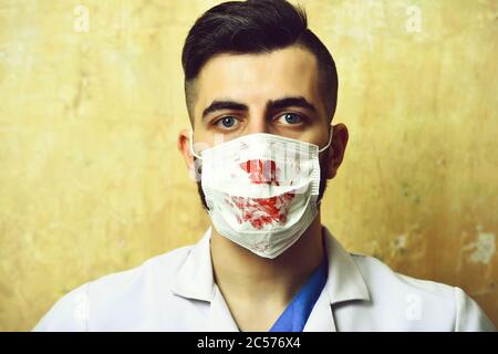 Arzt mit stilvollem Haarschnitt und Prozedurmaske mit Blut auf beigem Hintergrund gefärbt. Konzept der Professionalität und Gesundheitsversorgung Stockfoto