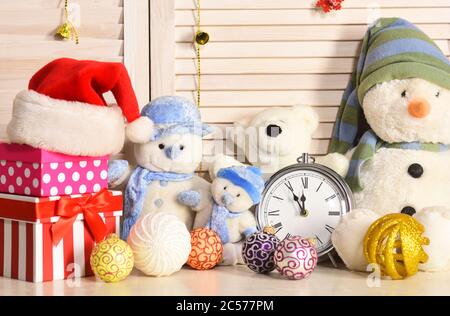 Spielzeug auf Büro auf Holzwand Hintergrund platziert. Schneemänner, Teddybären, Weihnachtskugeln und Geschenkboxen in der Nähe des Weckers. Dekor-Konzept für Feiern und Neujahr. Weihnachtsdekoration im festlichen Raum Stockfoto