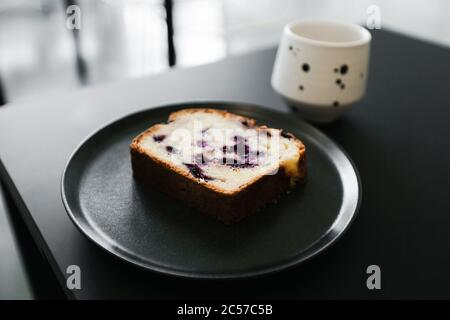 Ein Stück Obstkuchen mit Beeren und eine Tasse Kaffee auf einem schwarzen Tisch Stockfoto