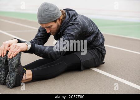 Motivierter junger fit Sportler, der auf der Stadion-Rennstrecke arbeitet, Stretching-Übungen macht Stockfoto